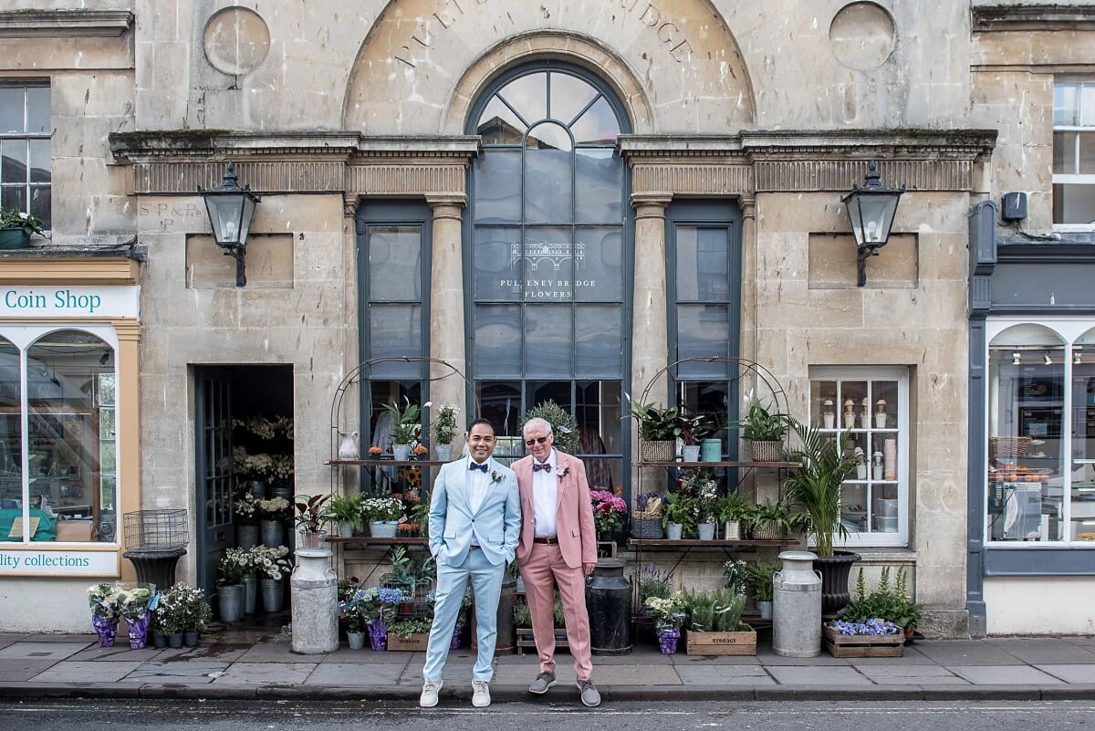 Newlywed gay couple posing in front of Bath Pulteney Bridge Flower shop